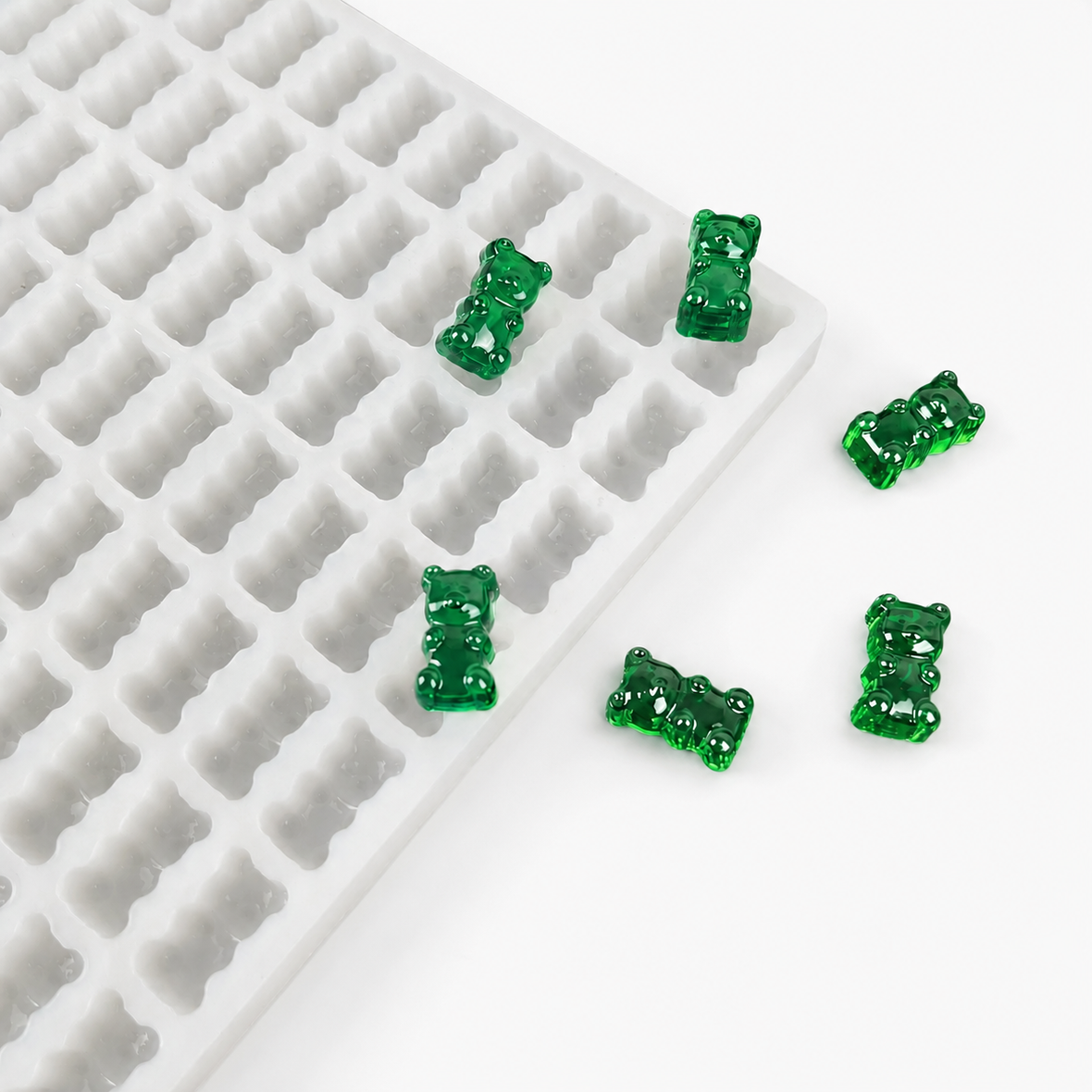 Finished emerald green gummy bears beside a commercial silicone gummy bear mold