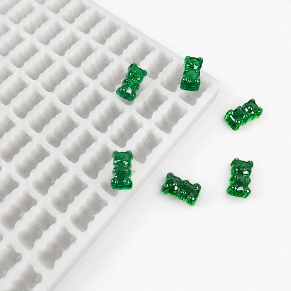 Finished emerald green gummy bears beside a commercial silicone gummy bear mold