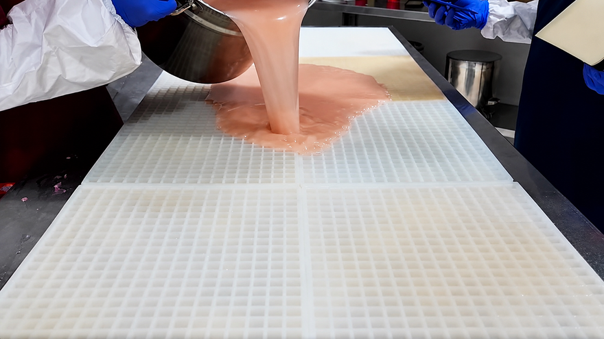 Zespół Gummy Molds wylewa masę żelkową na dużą komercyjną silikonową formę przed zgarnięciem nadmiaru