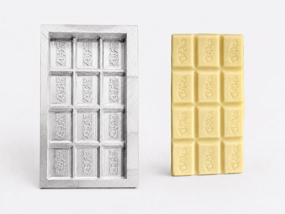 Single-cavity aluminum chocolate bar prototype beside a finished white chocolate test bar